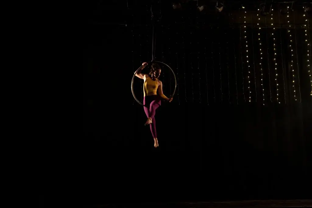 Artista de acrobacia aérea en aro sobre escenario oscuro con luces