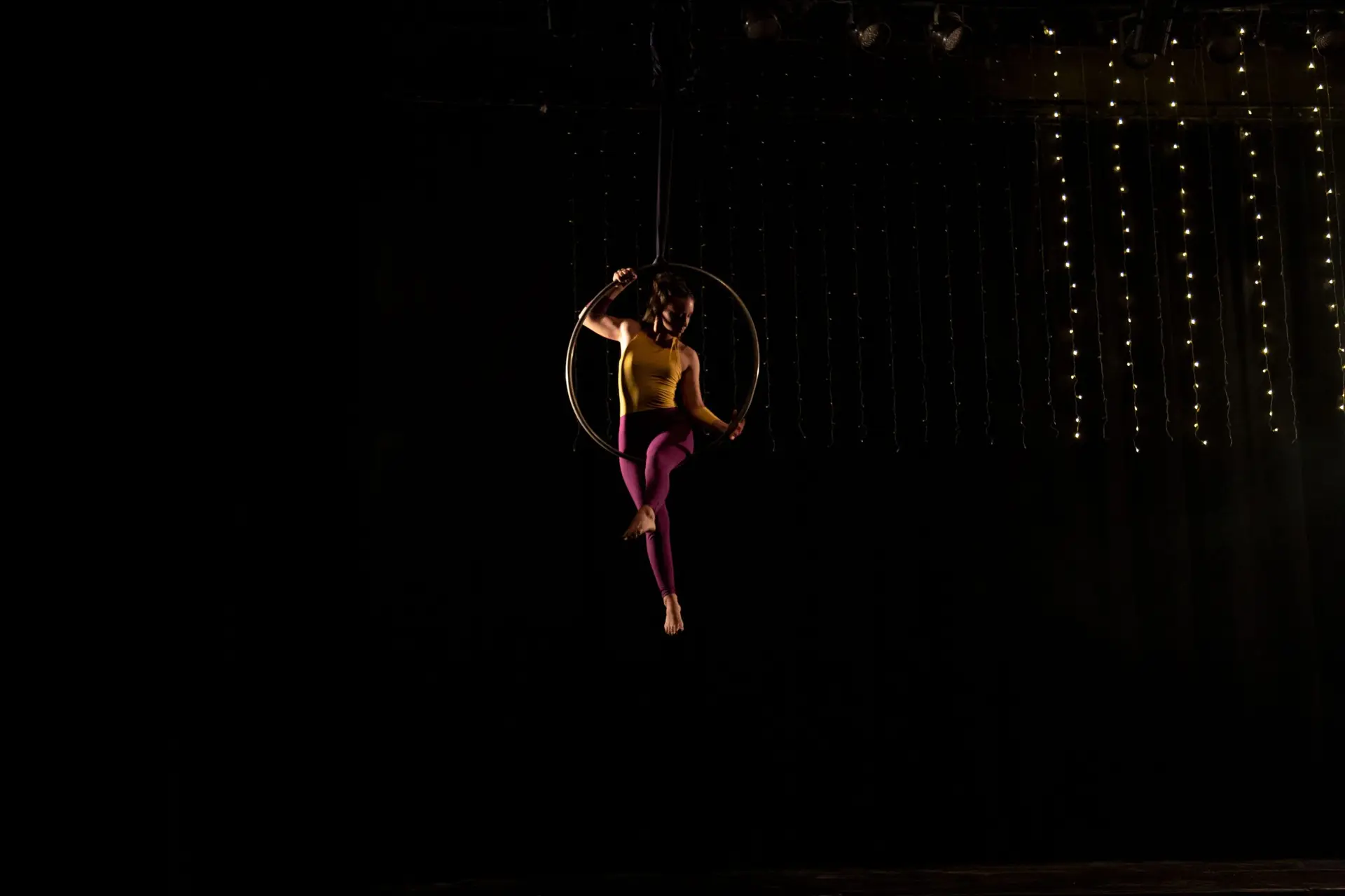 Artista de acrobacia aérea en aro sobre escenario oscuro con luces